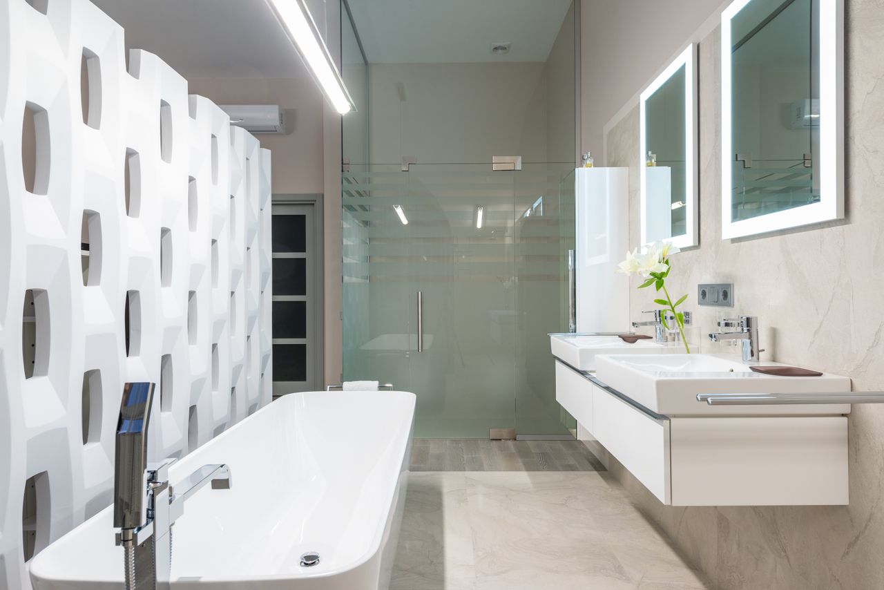 White bathtub with tap near decorative partition placed near sink and mirrors in stylish light bathroom with glass shower cabin